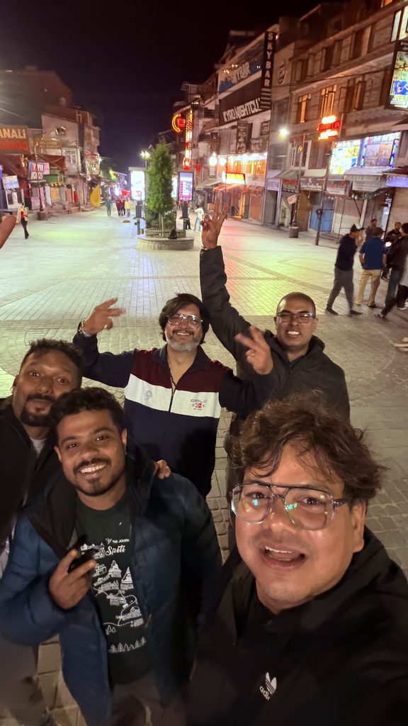 Group of friends enjoying a night selfie at Mall Road Manali with lit shops and street lights in the background