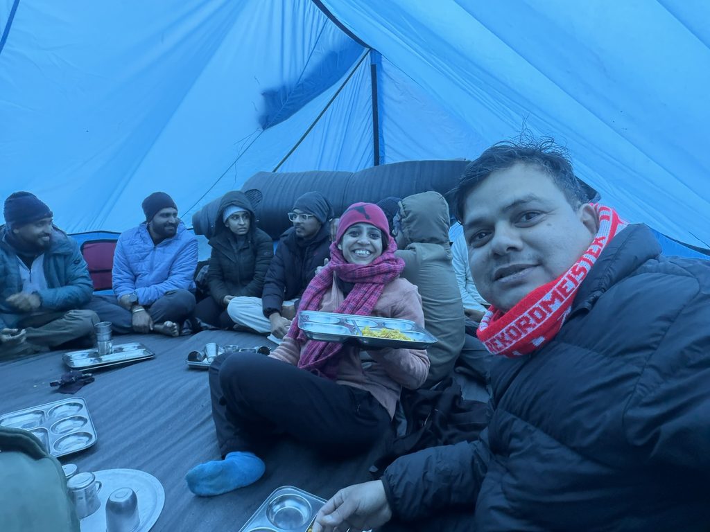 Trekkers sharing a meal inside a blue tent at Dhanderas Thatch campsite during the Rupin Pass trek