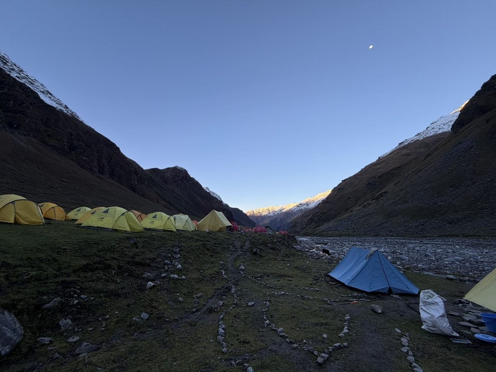 Yellow and blue trekking tents at Dhanderas Thatch beneath a clear evening sky and surrounding Himalayan peaks.