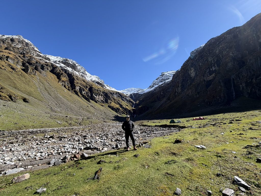 Trekker standing in a rocky Himalayan valley surrounded by snow-covered peaks during the Rupin Pass trek